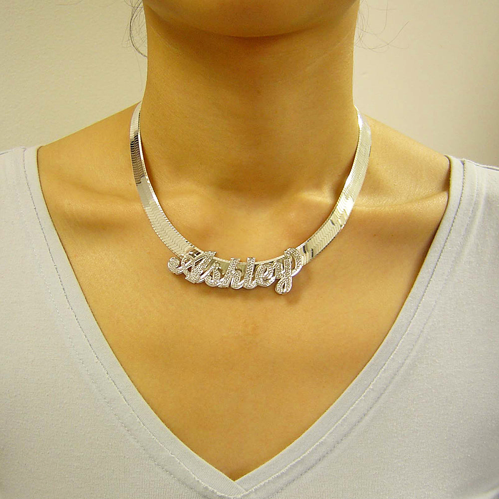 Model wearing a personalized sterling silver 3D nameplate pendant on a thick herringbone chain.