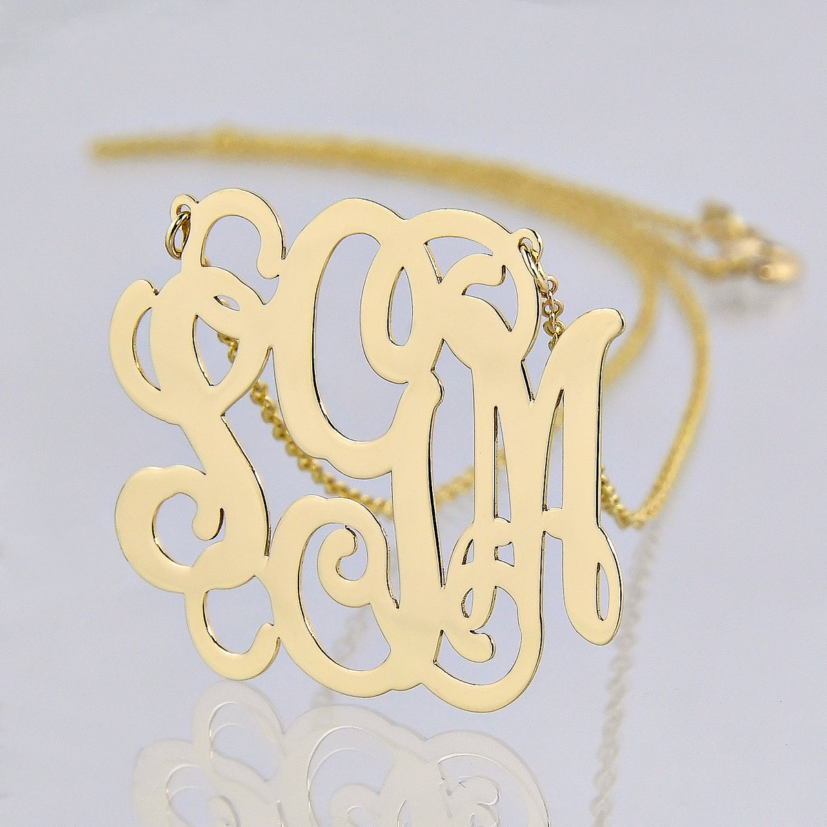 Close-up of a custom solid gold 3 initial monogram necklace.