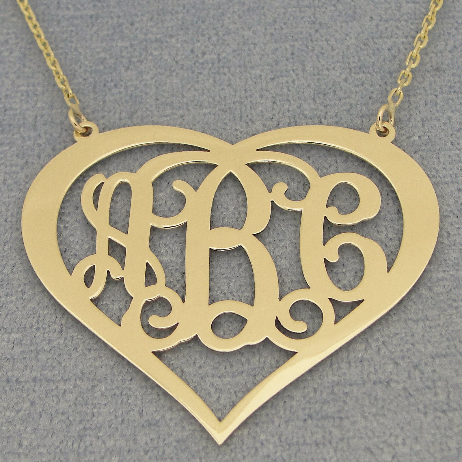 Close-up of a custom yellow solid gold three-initial heart monogram pendant on a gray background