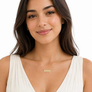 Woman wearing a dainty solid yellow gold mommy nameplate necklace with a fine chain and white top.
