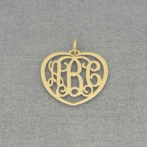 Close-up of a small gold heart monogram pendant with three custom initials on a gray background.