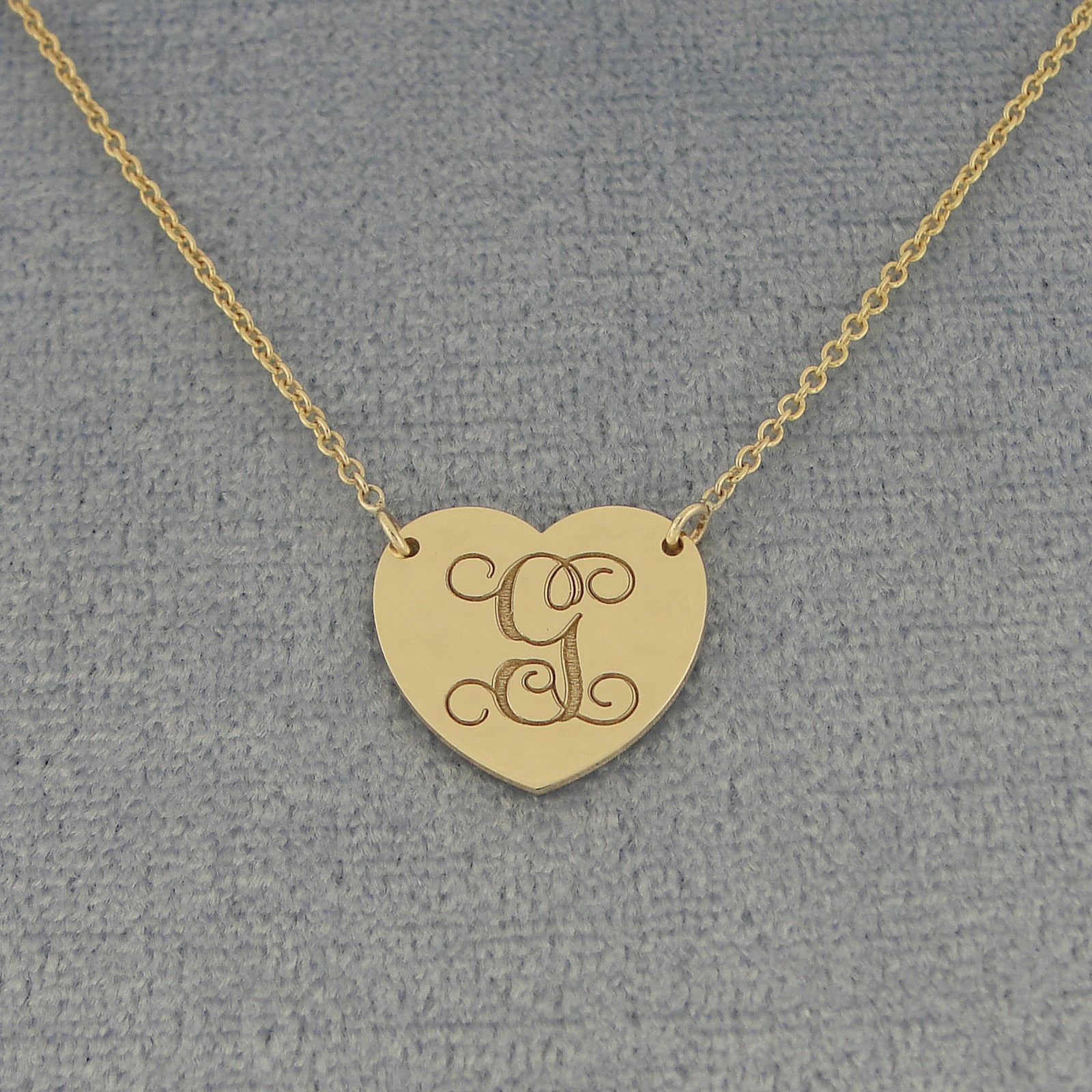 Custom solid gold heart-shaped pendant with an engraved cursive monogram letter G on a textured background.