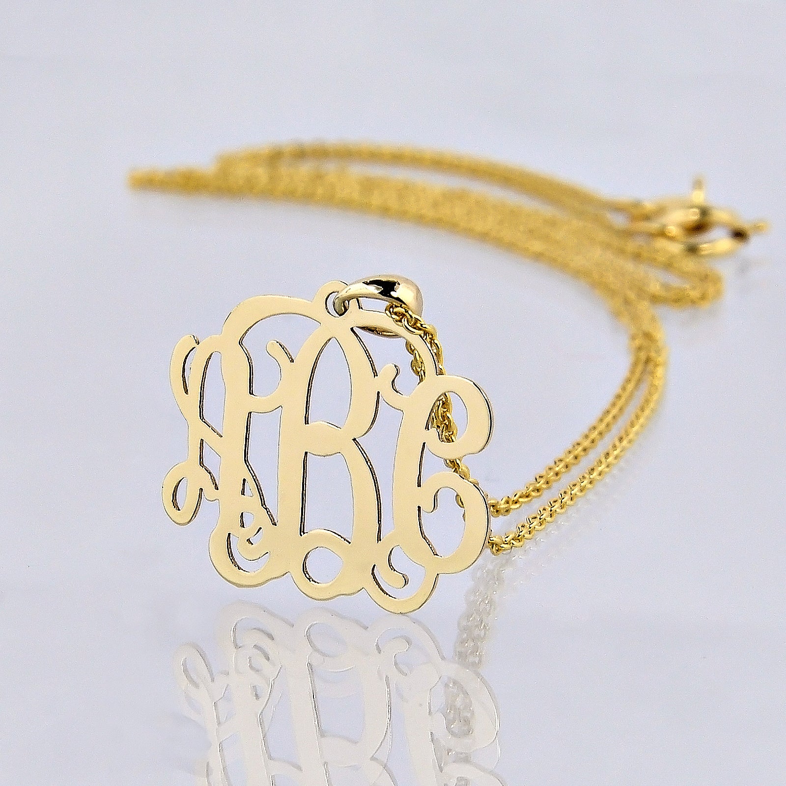 10k or 14k solid yellow gold mini three-initial monogram pendant necklace with a reflection on a white background.