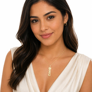 Woman wearing a gold vertical KING crown name pendant on a chain with a white V-neck top