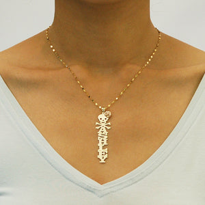 Close-up of an Ashley gold vertical name pendant with skull, crossbones, and rose detail, worn on a chain above a white V-neck top.