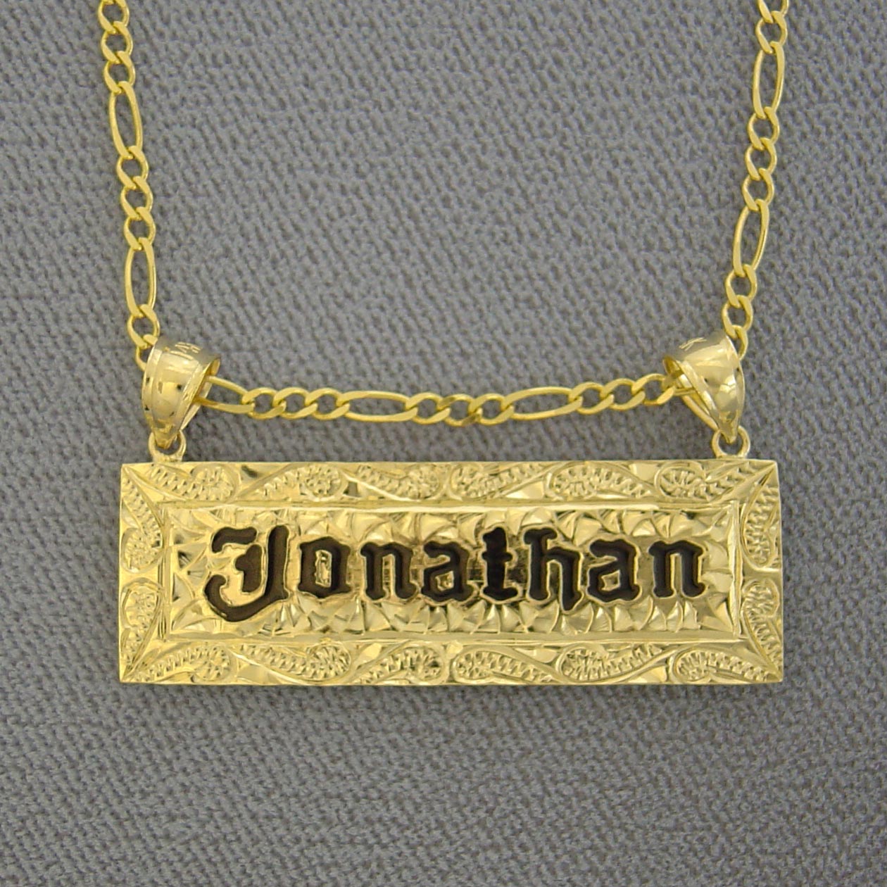 Detailed close-up of hand-engraved Hawaiian scrollwork and black enamel name engraving on a solid gold pendant.