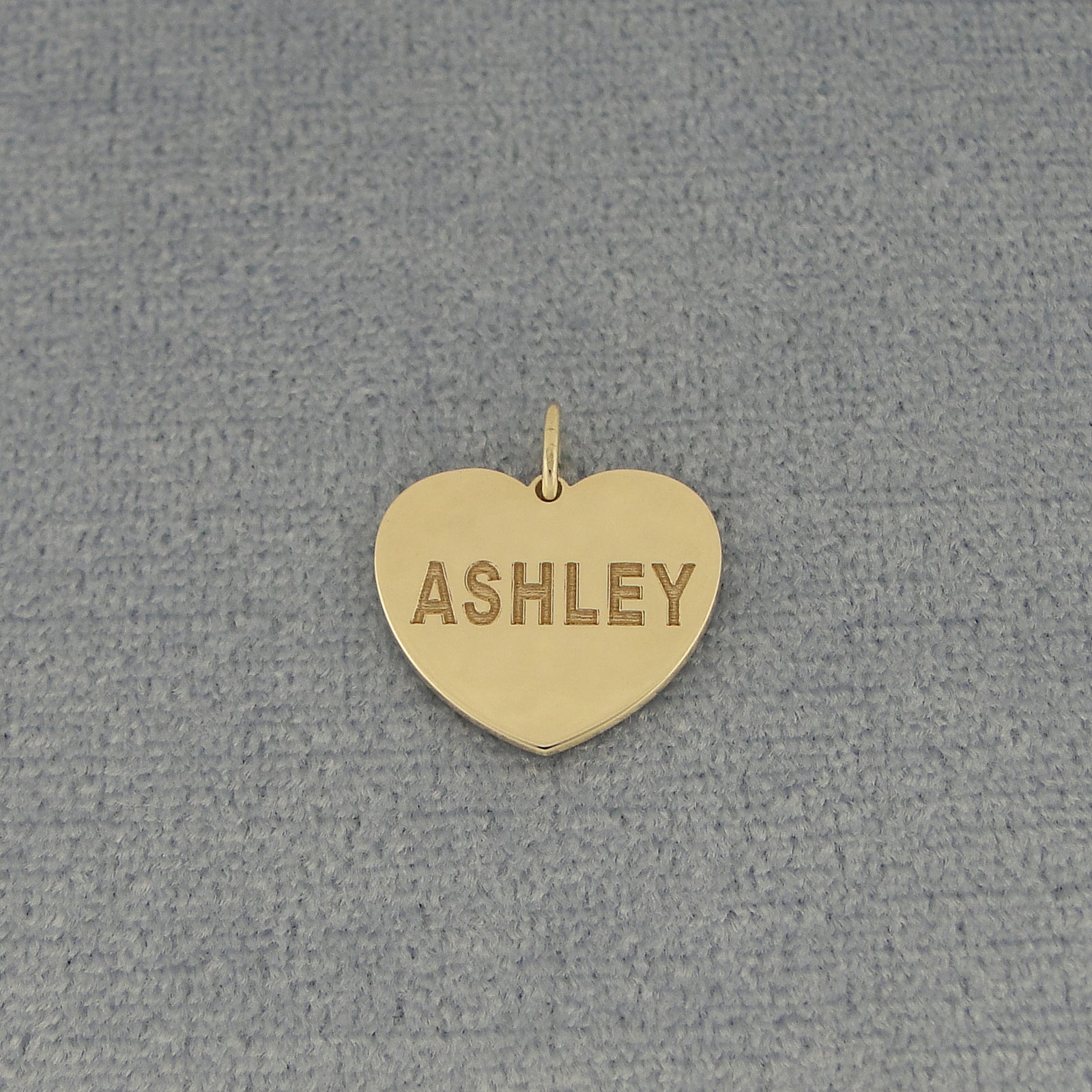 Personalized yellow gold heart charm pendant engraved ASHLEY on textured gray fabric