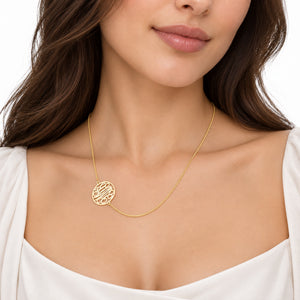 Close-up of a small solid gold three-initial monogram necklace worn by a woman