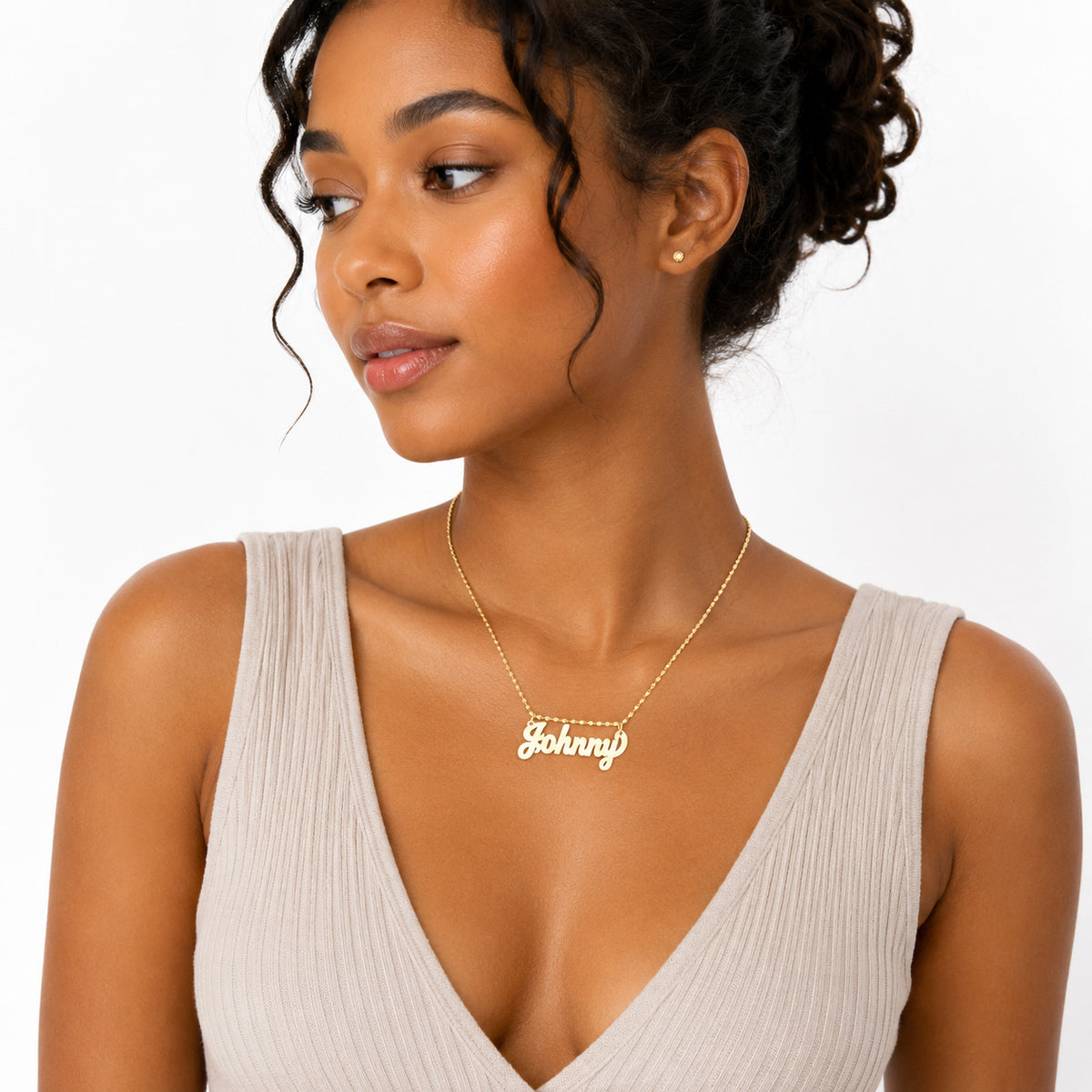 A woman wearing a delicate gold nameplate necklace that reads 'Johnny' on a white background.
