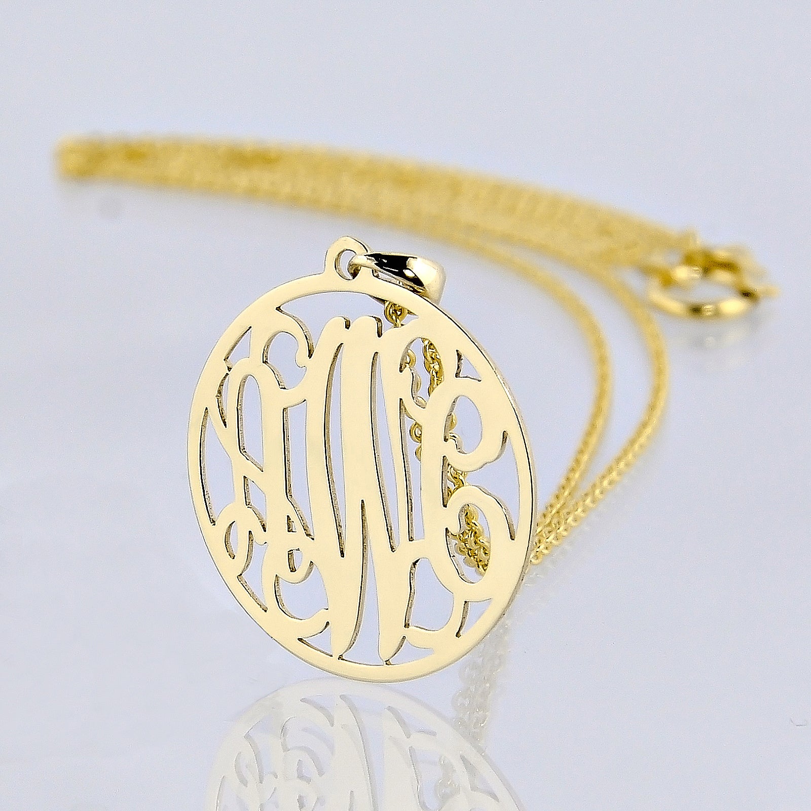 Custom solid gold 3-initial circle monogram pendant necklace on a matching gold chain against a reflective white surface.
