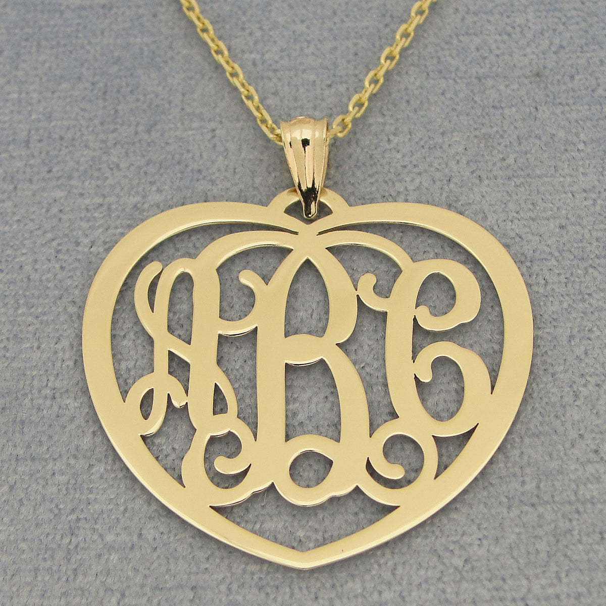 Yellow gold 3-initial heart monogram pendant necklace on a textured gray background.