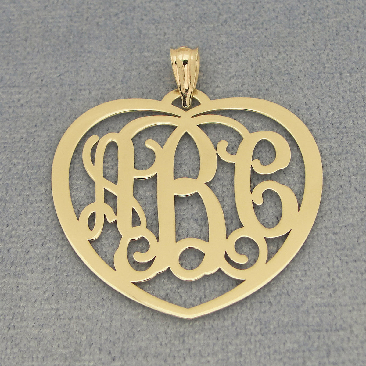 Yellow gold 3-initial heart monogram pendant with openwork initials on a textured gray background.