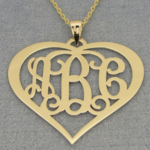 Solid gold 3-initial heart monogram necklace with a chain on a gray background.