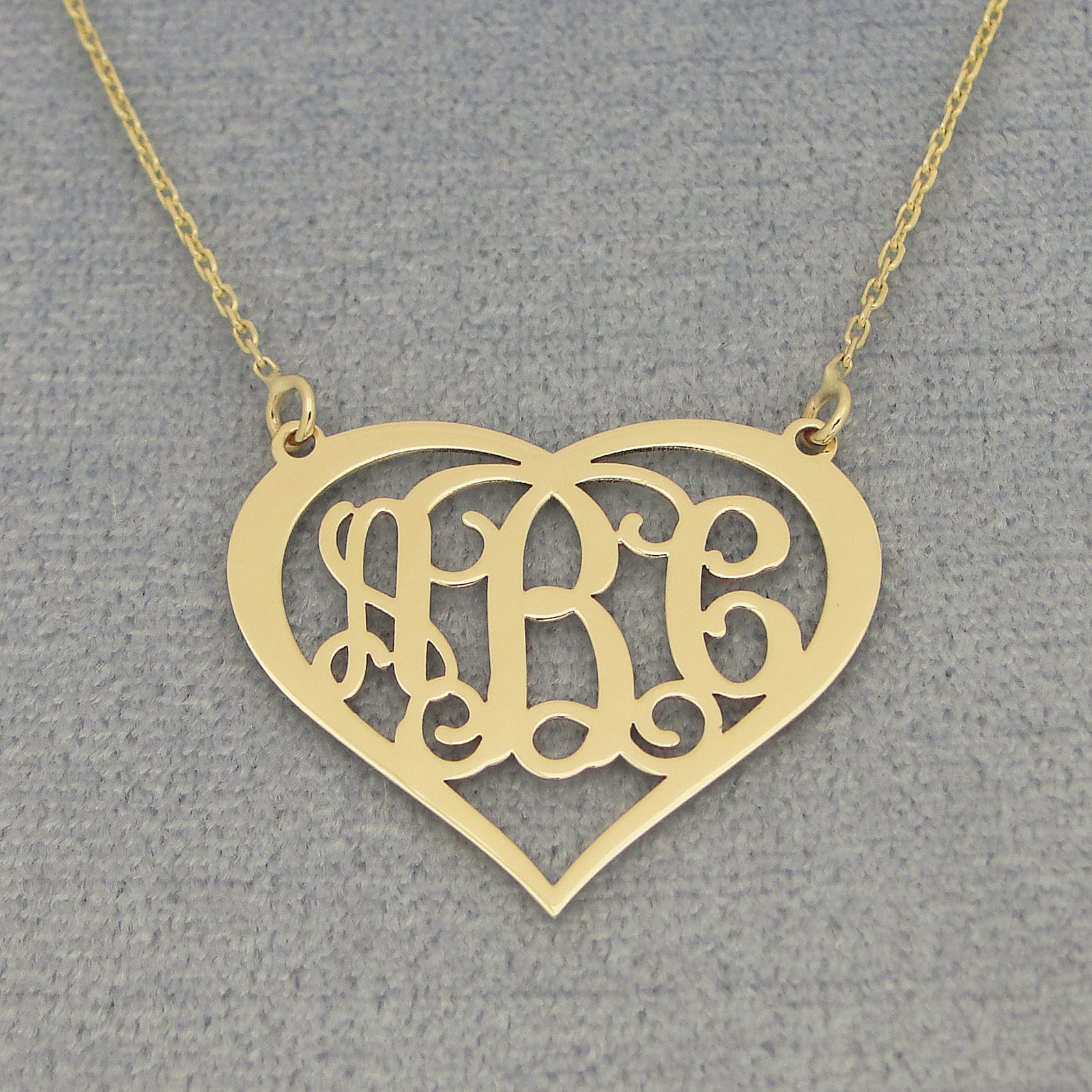 Close-up of personalized solid gold heart pendant with three-initial script monogram