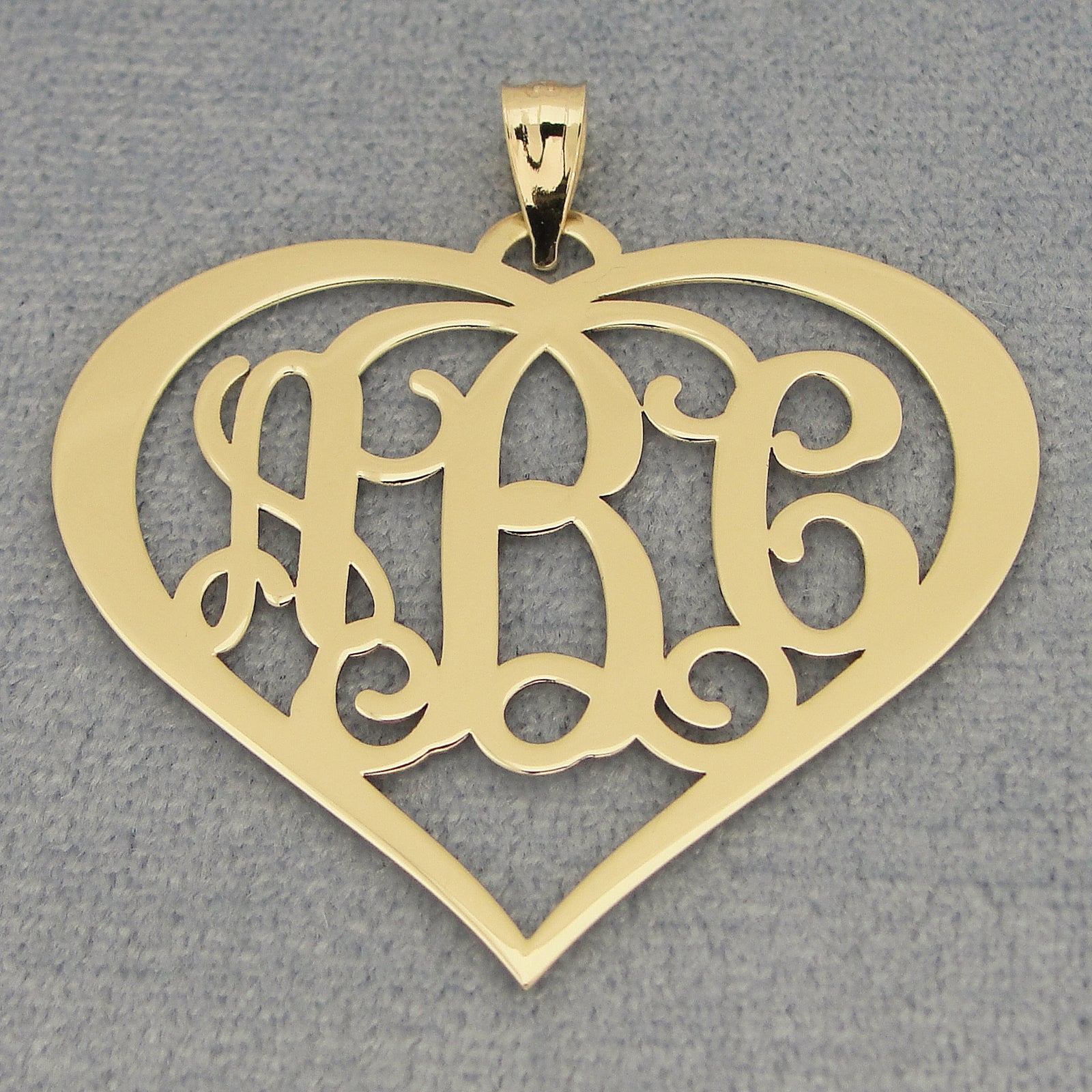 Close-up of a solid gold 3-initial heart monogram pendant on a gray background.