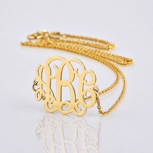 Close-up of a solid 14k yellow gold three-initial sideways monogram necklace with a soft reflection