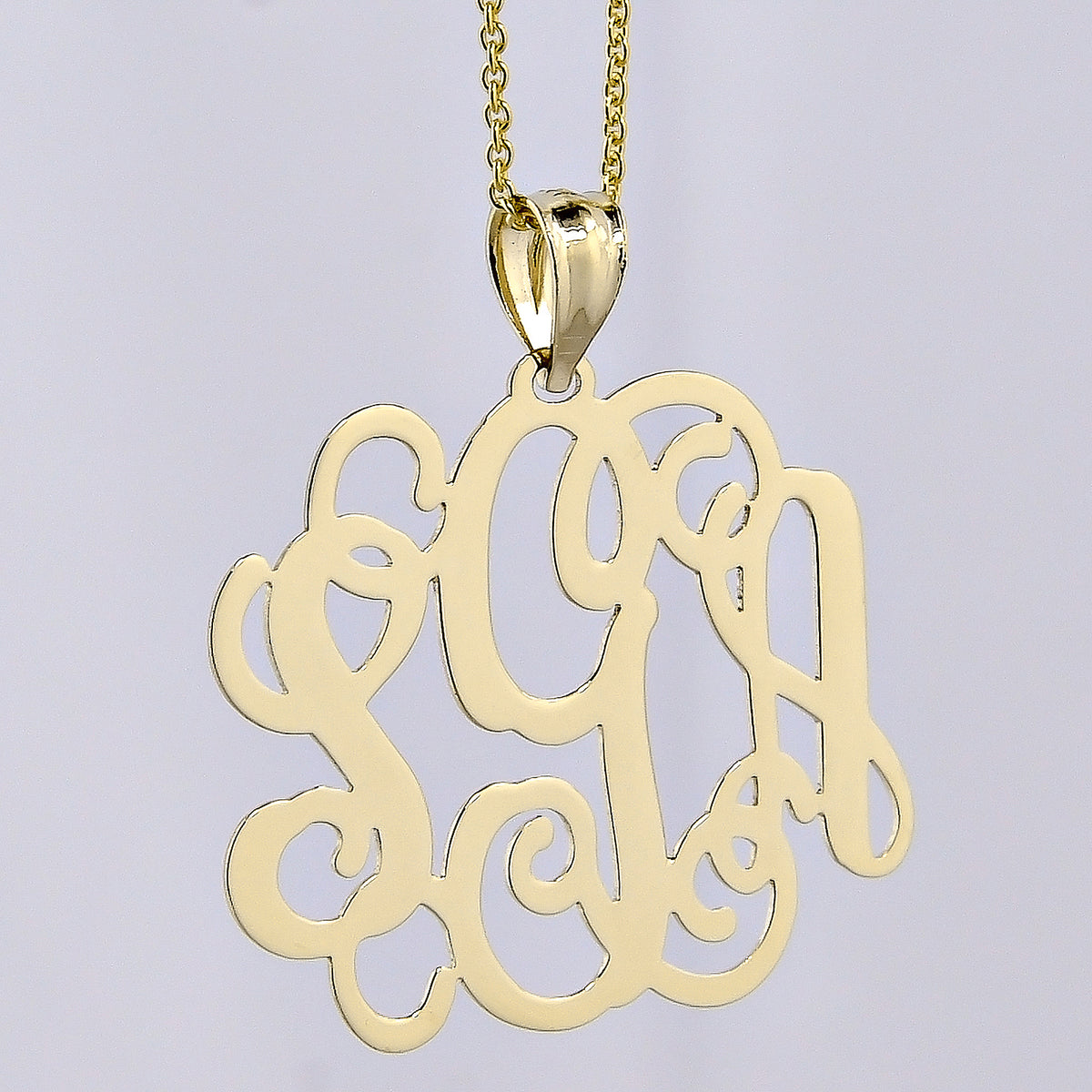 Close-up front view of a solid yellow gold three-initial custom monogram pendant on a fine chain.