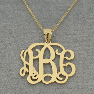 Solid yellow gold three-initial monogram pendant on a fine chain against a gray jewelry background.