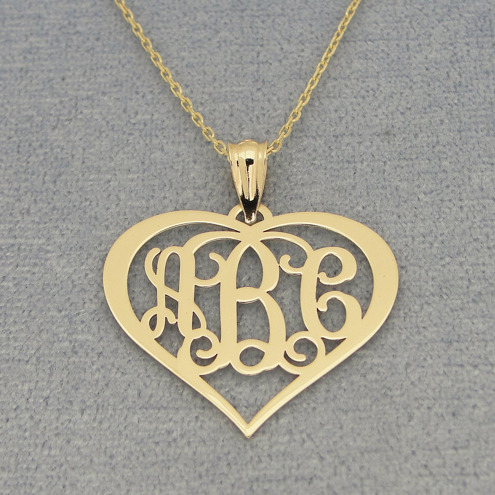 Detailed view of personalized solid gold heart monogram necklace with three initials