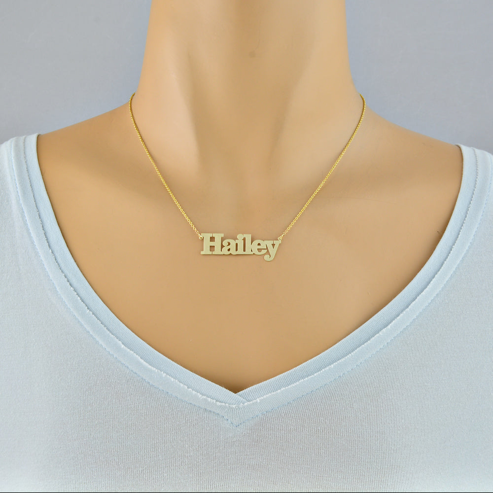 Woman wearing a custom 14k solid gold block font nameplate necklace handcrafted in Los Angeles.