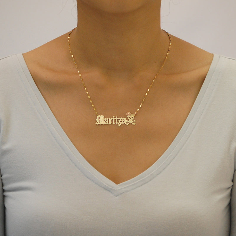 Woman wearing a personalized 16-inch 14k gold Old English name necklace with a skull pendant detail.