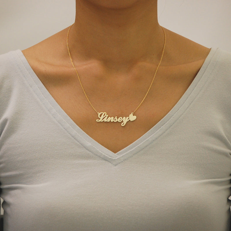 Woman wearing a customized solid gold script nameplate necklace with a heart end.