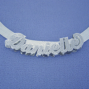 Close-up view of the diamond-accented 3D cursive script nameplate slider on a textured blue background.