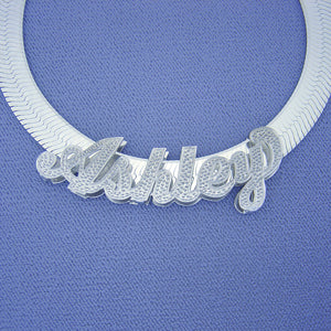 Custom sterling silver 3D "Ashley" name pendant with diamond accents displayed on a blue neck bust with a herringbone chain.