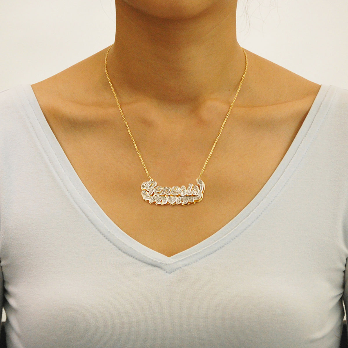 Custom 14k gold iced-out nameplate necklace featuring angel wings and heart detail, worn on a model's neck.