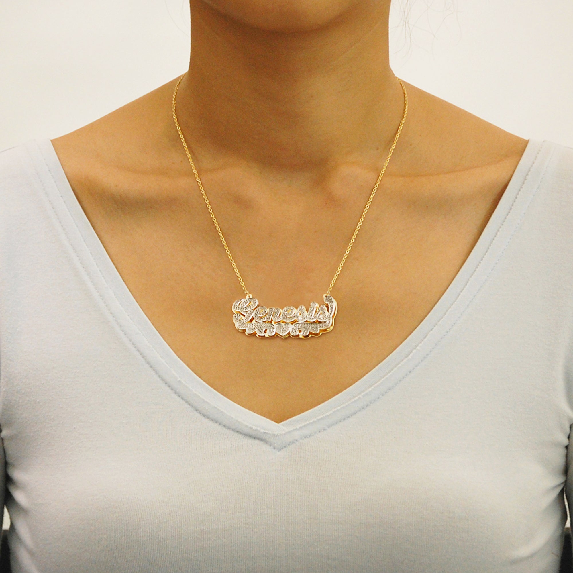 Custom 14k gold iced-out nameplate necklace featuring angel wings and heart detail, worn on a model's neck.