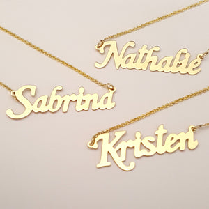 Stack of personalized solid gold nameplate necklaces featuring script names Sabrina and Kristen.