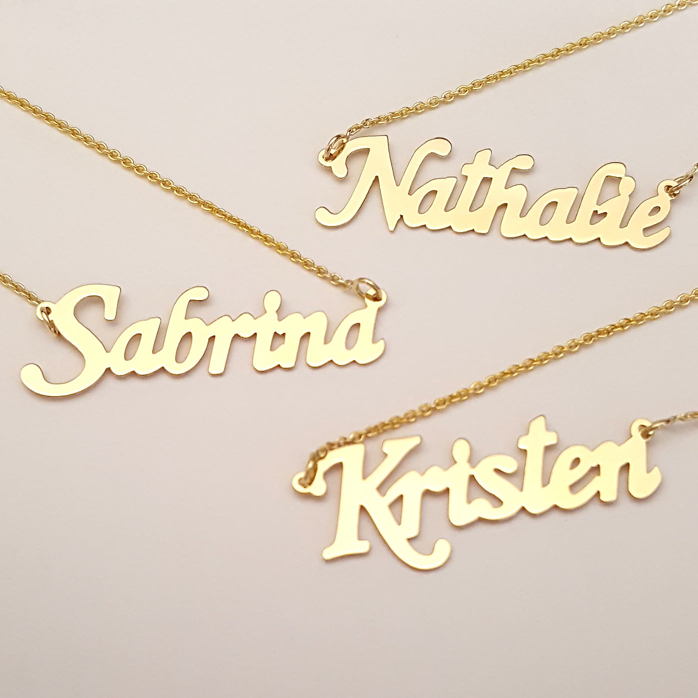 Stack of personalized solid gold nameplate necklaces featuring script names Sabrina and Kristen.