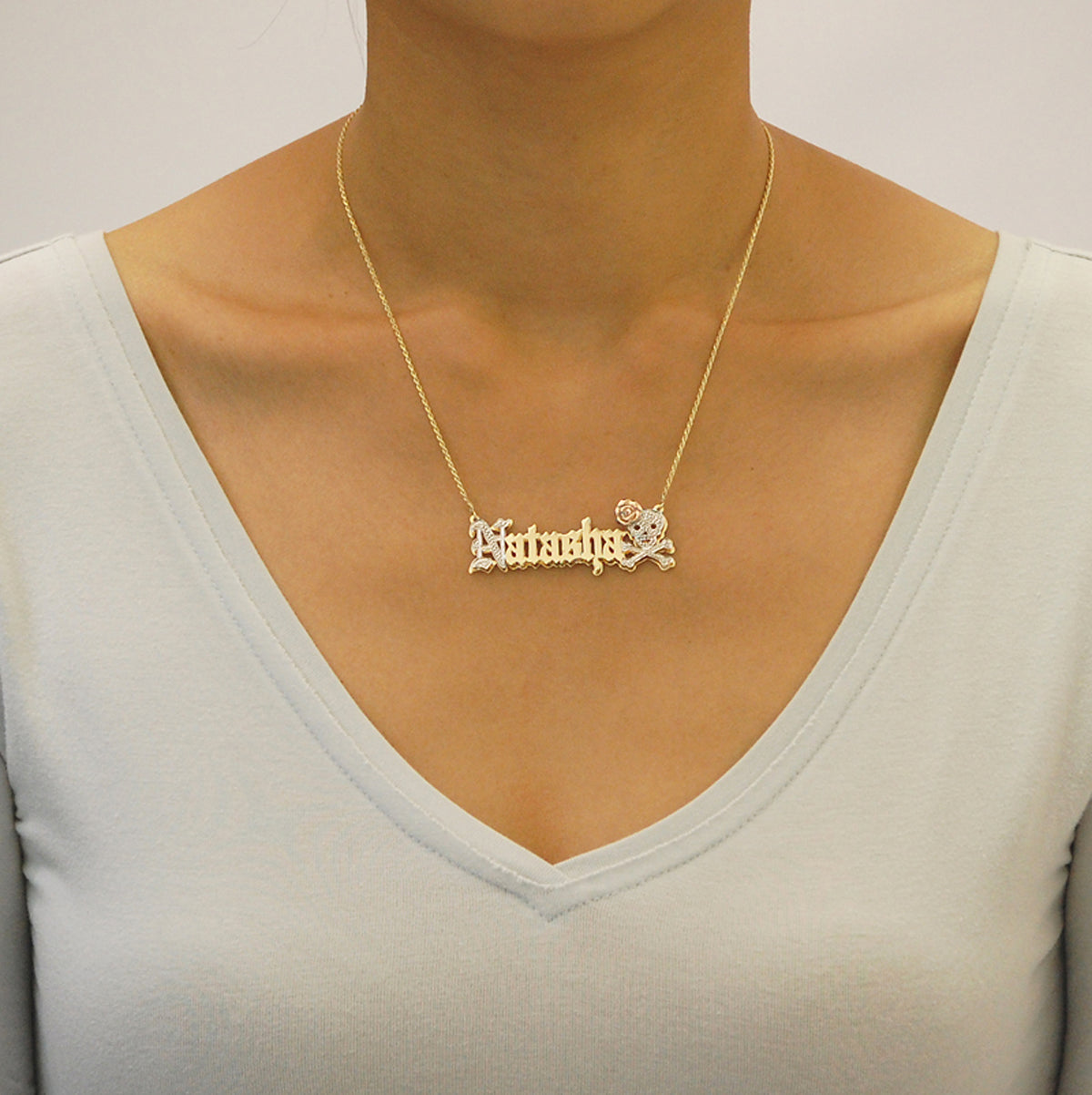 Woman wearing a personalized 10k solid gold Old English nameplate necklace with skull crossbones accent.