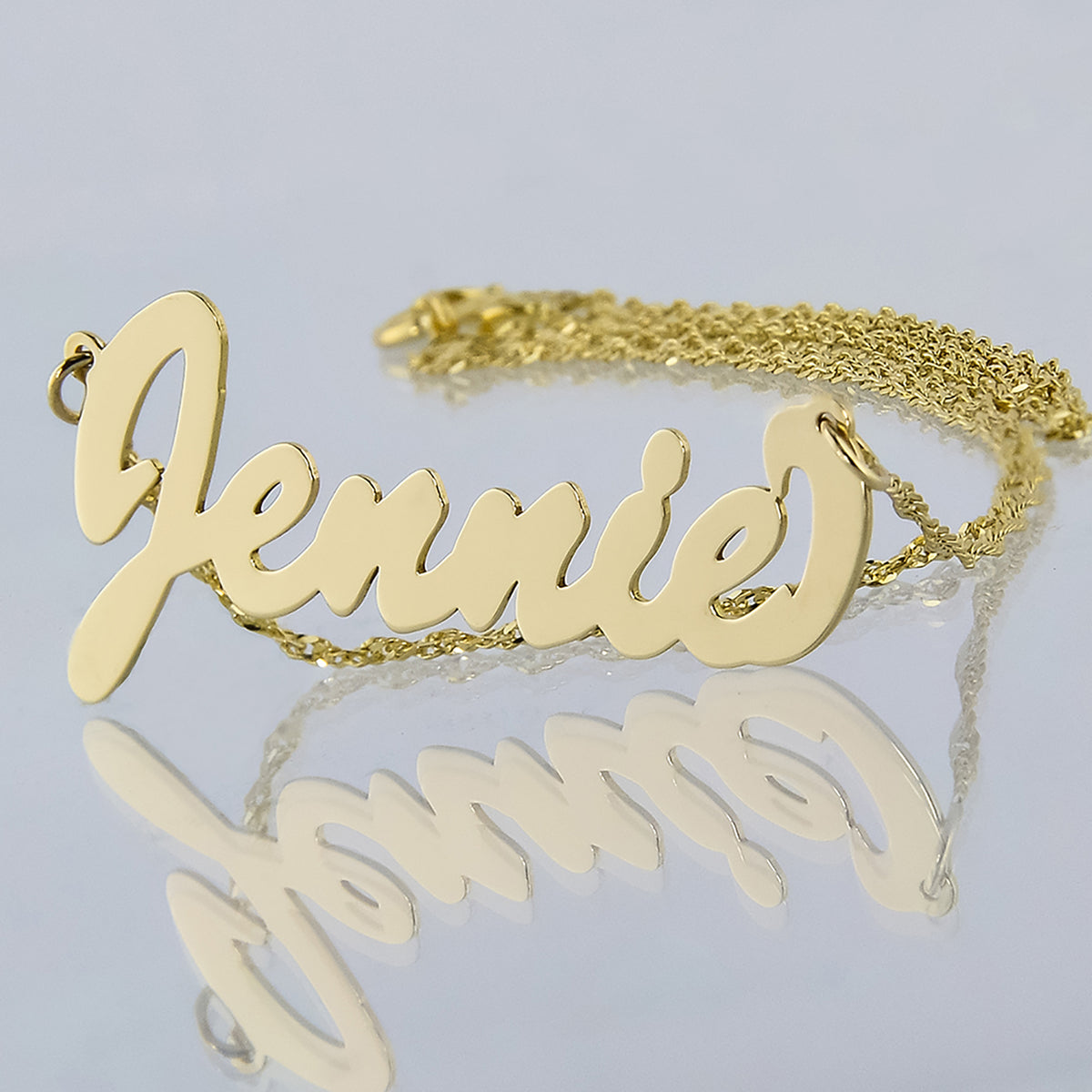 Detailed close-up of a small solid gold cursive nameplate spelling Jennie.