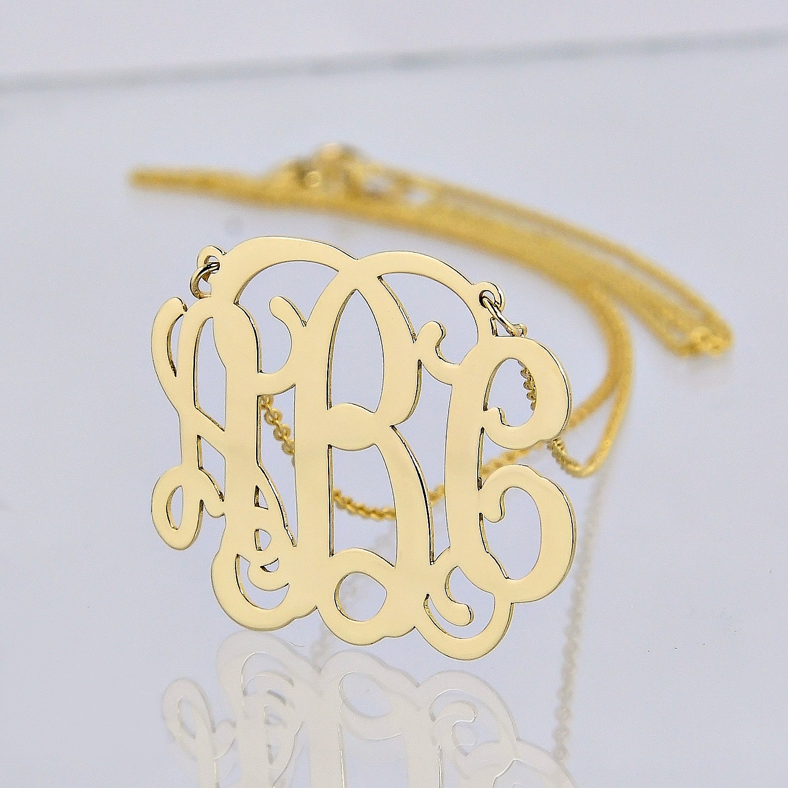 Close-up of a personalized solid gold 3-initial monogram necklace with a gold chain.